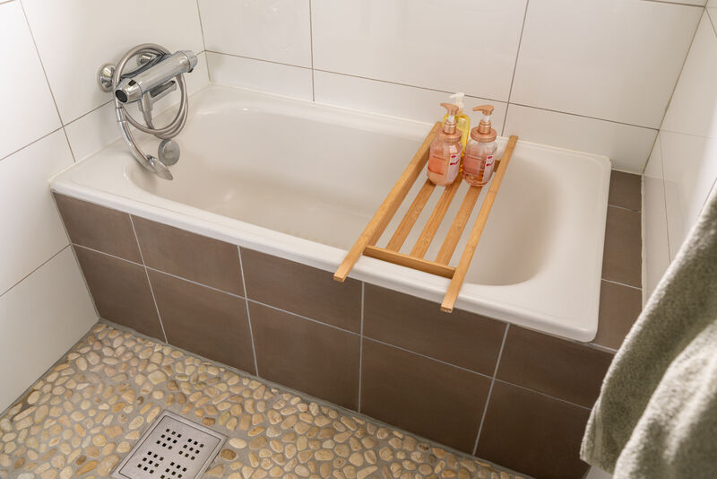 Baderommet er utstyrt med innmurt badekar og dusjsone med elvesten på gulv.